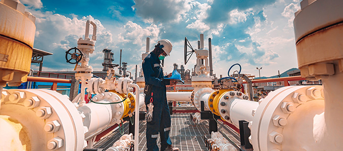 worker inspecting valves in industrial facility with blue sky and clouds showing process safety and efficiency in operations 4 key standards