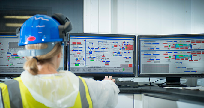 worker in safety gear looking at multiple computer screens displaying complex data related to operations and efficiency in a control room monitoring system five key metrics