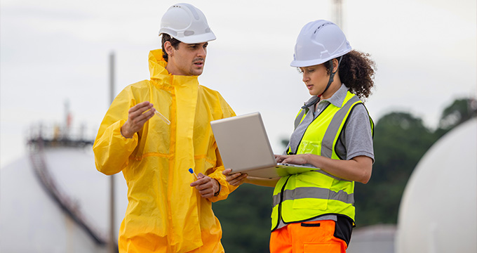 two construction workers discussing project details wearing safety gear while using a laptop in an industrial setting