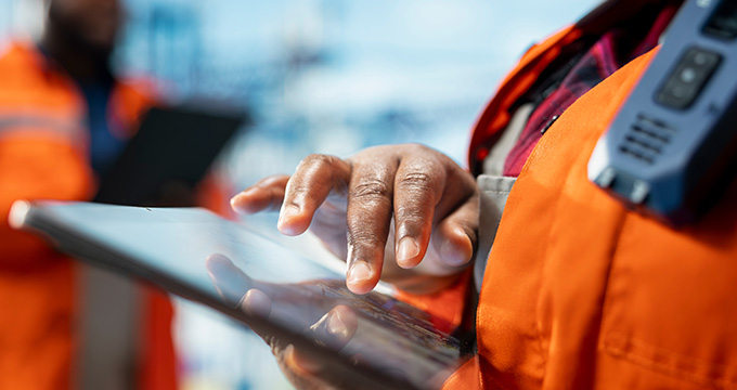 a person wearing an orange jacket using a tablet device with hands engaged in work and collaboration in an industrial setting for communication and productivity